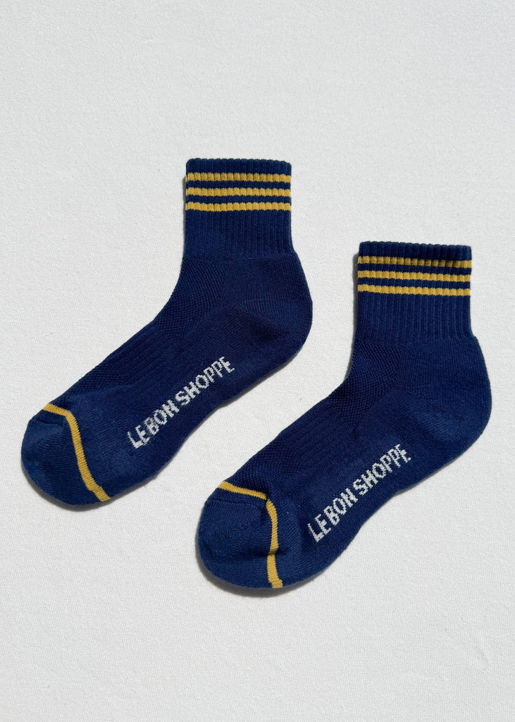 Pair of blue socks with yellow accents and 'Le Bon Shoppe' branding on a light gray background