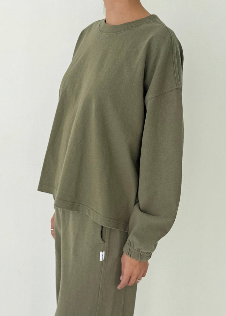 Person wearing an olive green long-sleeve shirt and pants on a plain background