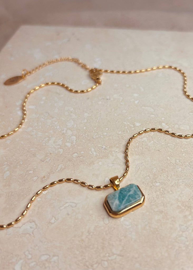 Gold necklace with a blue pendant on a beige surface