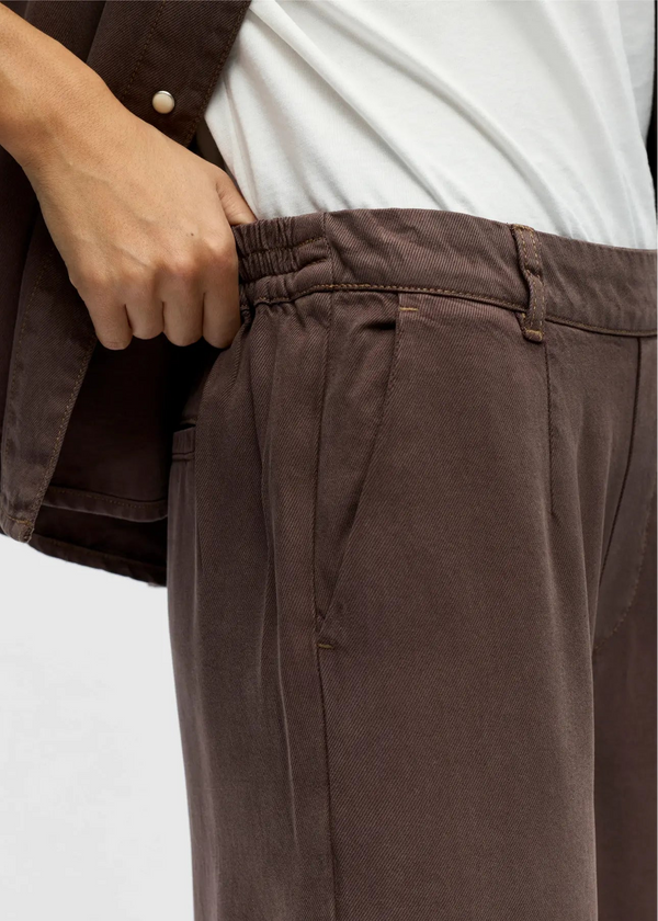 Brown pleated pants worn by a person on a white background