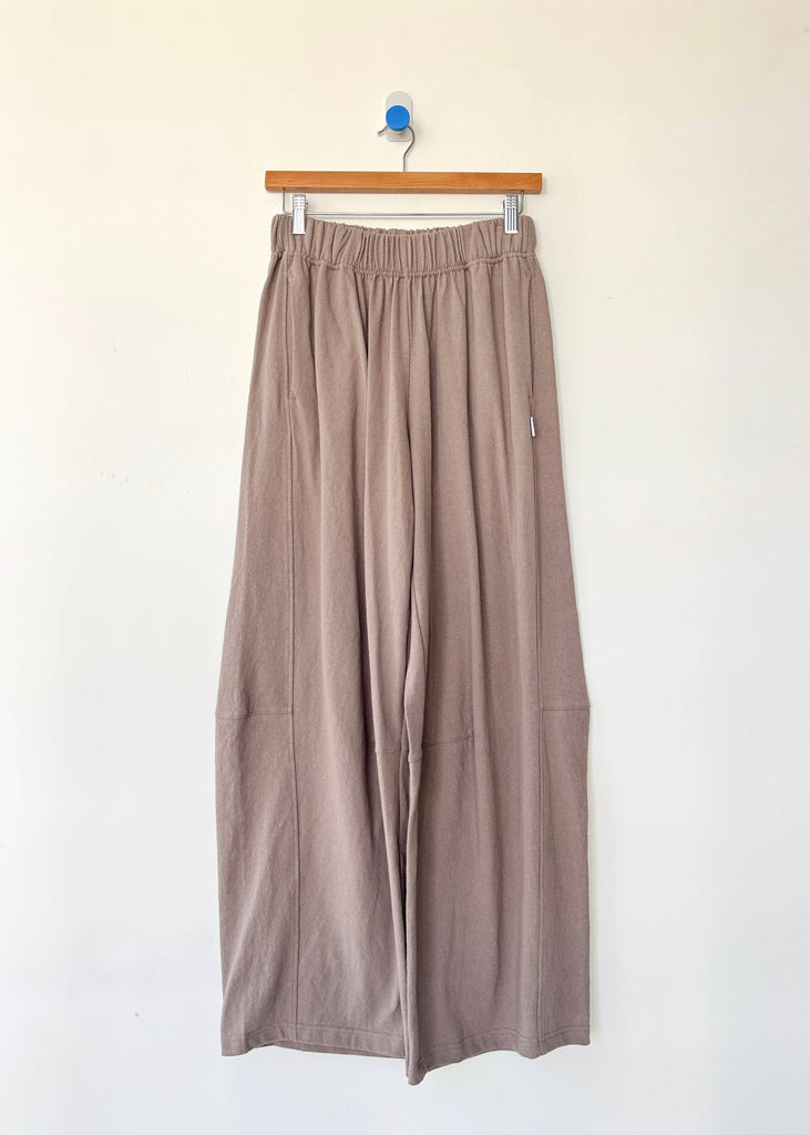 Beige wide-leg pants hanging on a wooden hanger against a white background