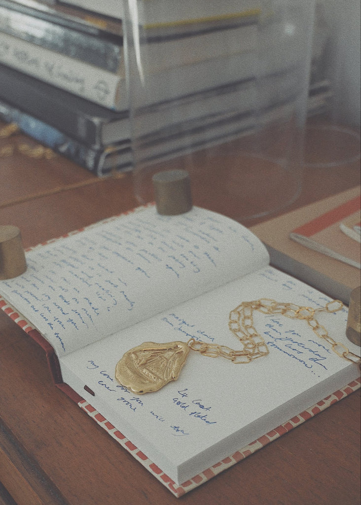 Open book with gold necklace and pendant on a wooden surface
