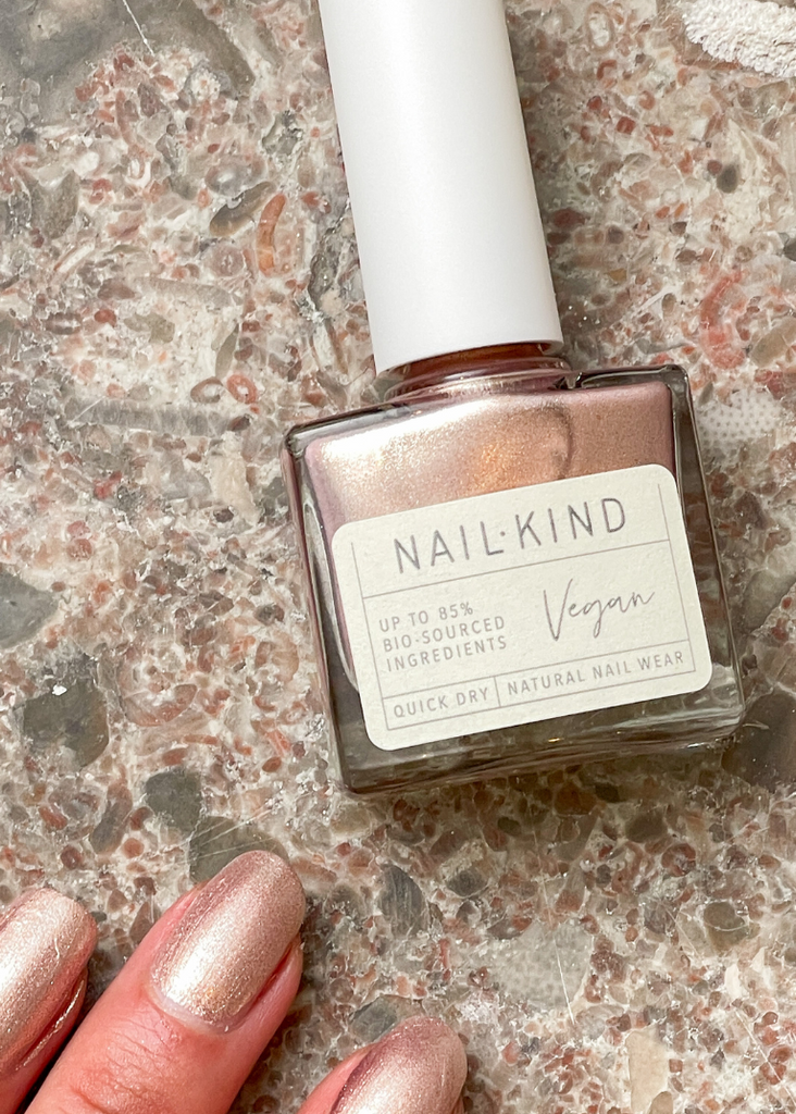 Nail polish bottle labeled 'NAILKIND' with a hand showing nails painted with a metallic nail polish on a textured surface.