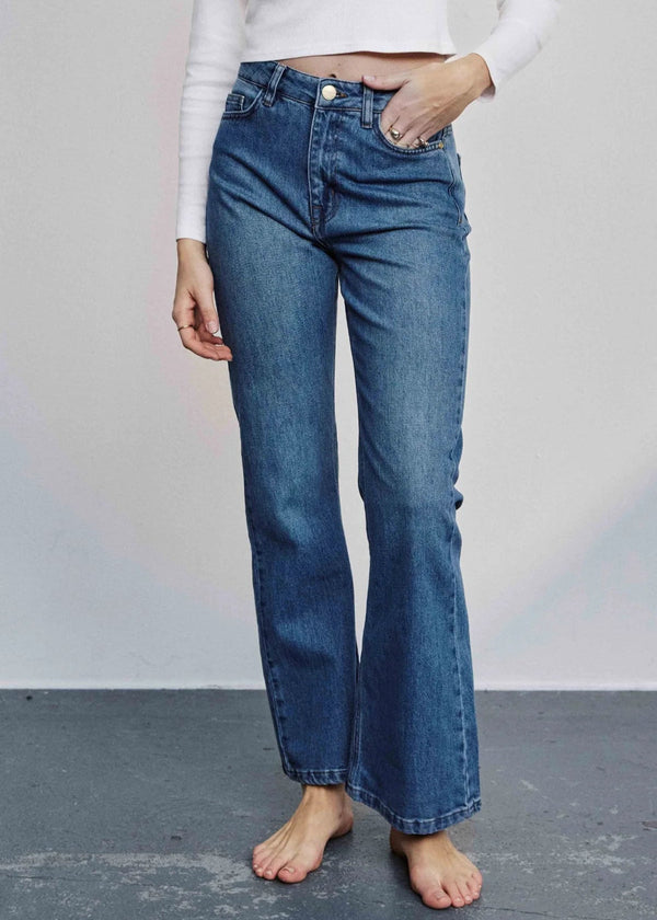 Person wearing blue jeans and a white top against a plain background