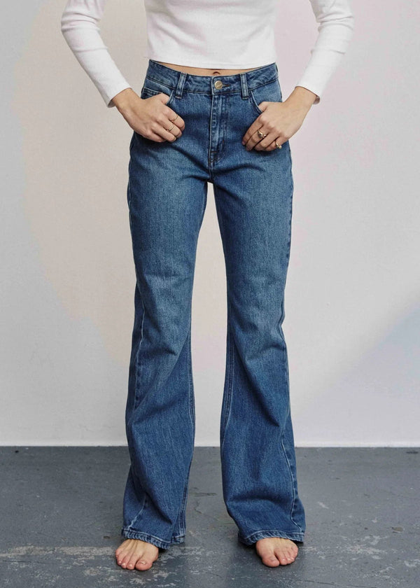 Person wearing blue jeans and a white top against a plain background