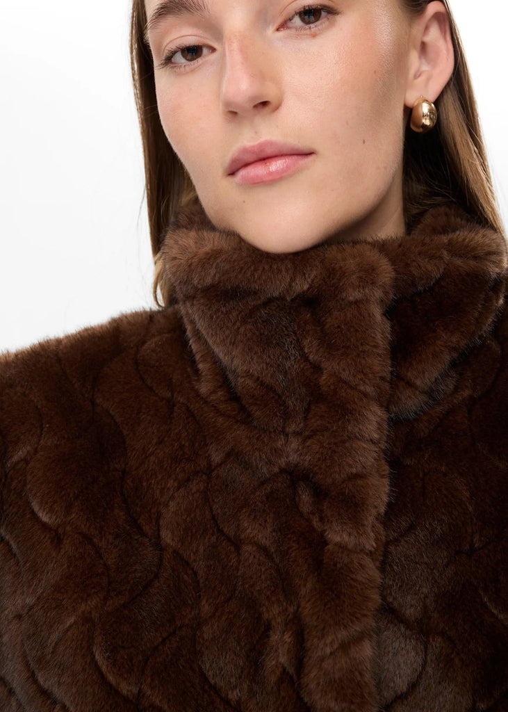 Close-up of a person wearing a brown fur garment with a plain background