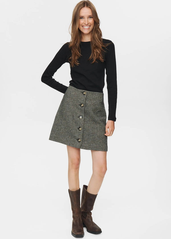 Woman wearing a black sweater and gray skirt with buttons on a white background