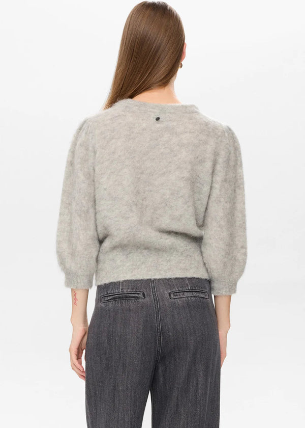 Woman wearing a gray sweater and dark pants on a white background