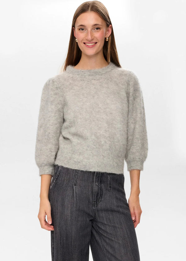 Woman wearing a gray sweater and dark jeans on a white background