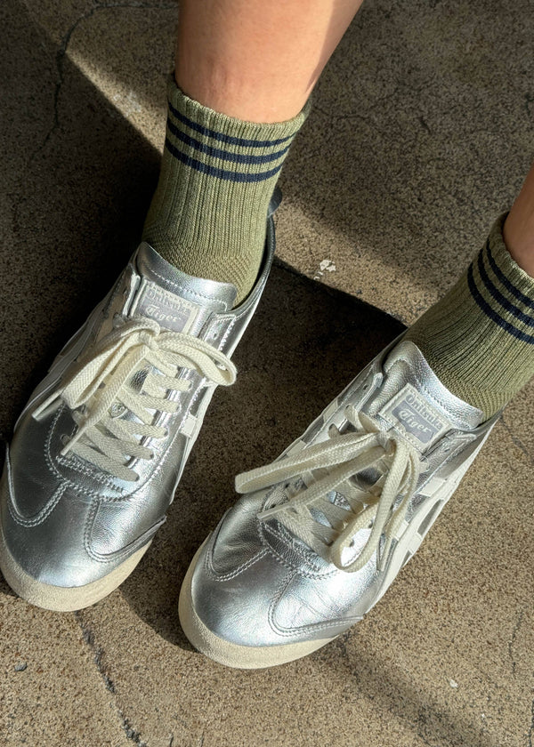 Silver sneakers worn with green striped socks on a concrete surface