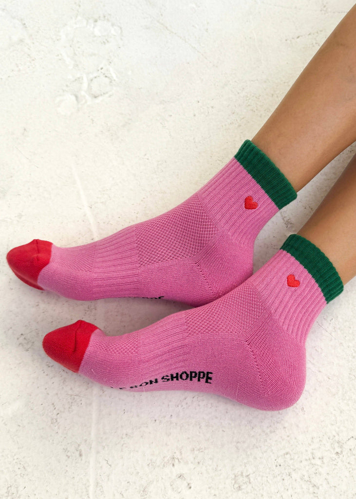Pink socks with red toes and green cuffs worn on a white surface