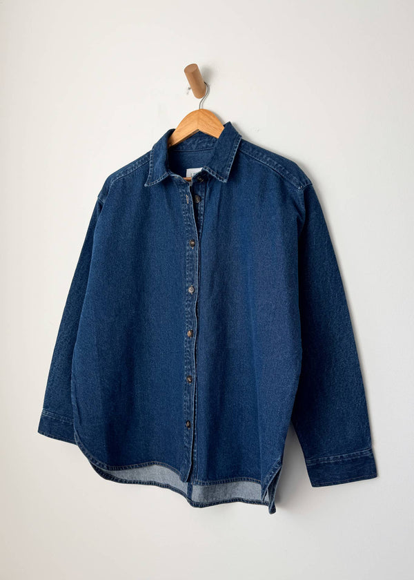 Blue denim shirt on a wooden hanger against a white background