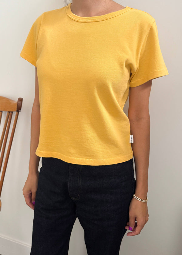 Person wearing a yellow t-shirt and black pants against a white wall.