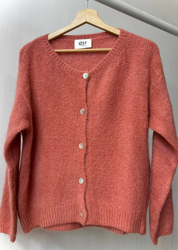 Pink cardigan on a hanger against a white wall