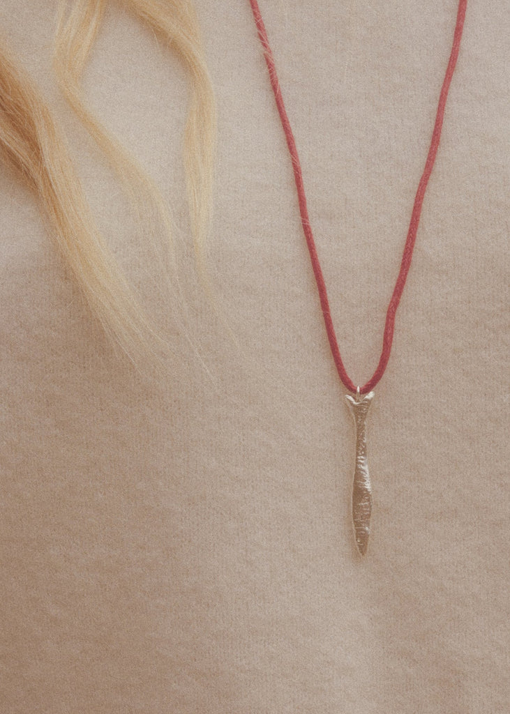 Necklace with a leaf-shaped pendant on a red cord against a beige background