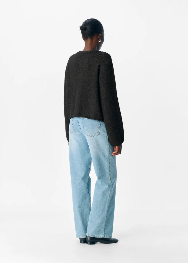Person wearing a black sweater and light blue jeans on a white background