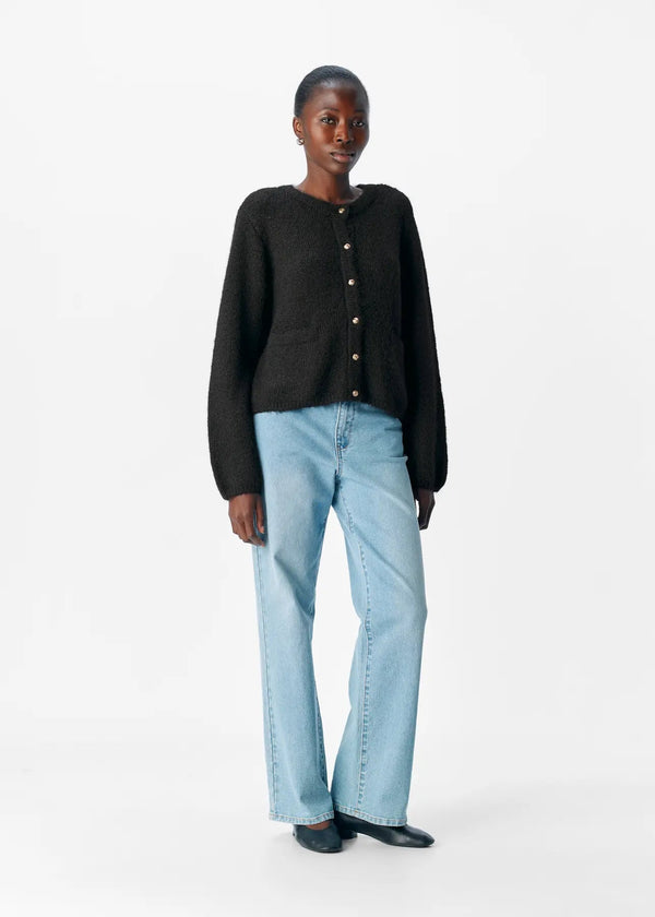 Person wearing a black cardigan and light blue jeans on a white background