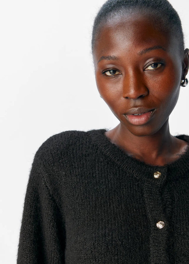 Woman wearing a black cardigan with gold buttons on a white background