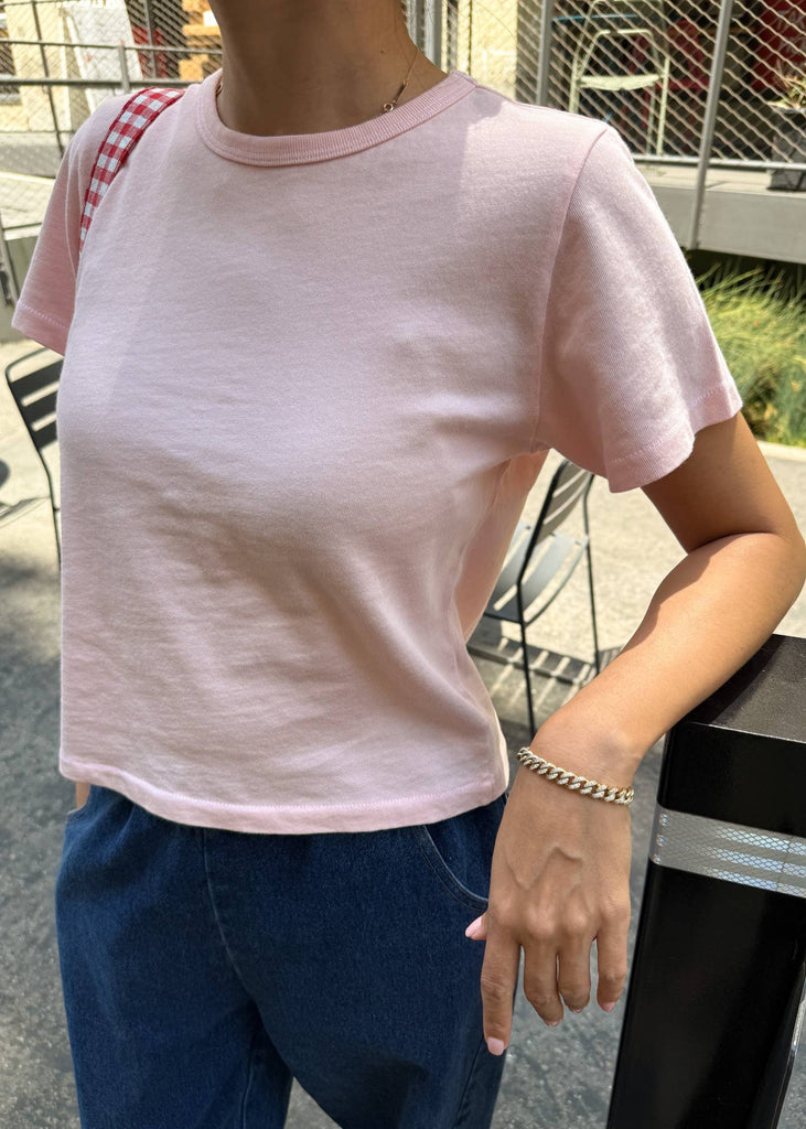 Person wearing a pink t-shirt and blue jeans standing outdoors.