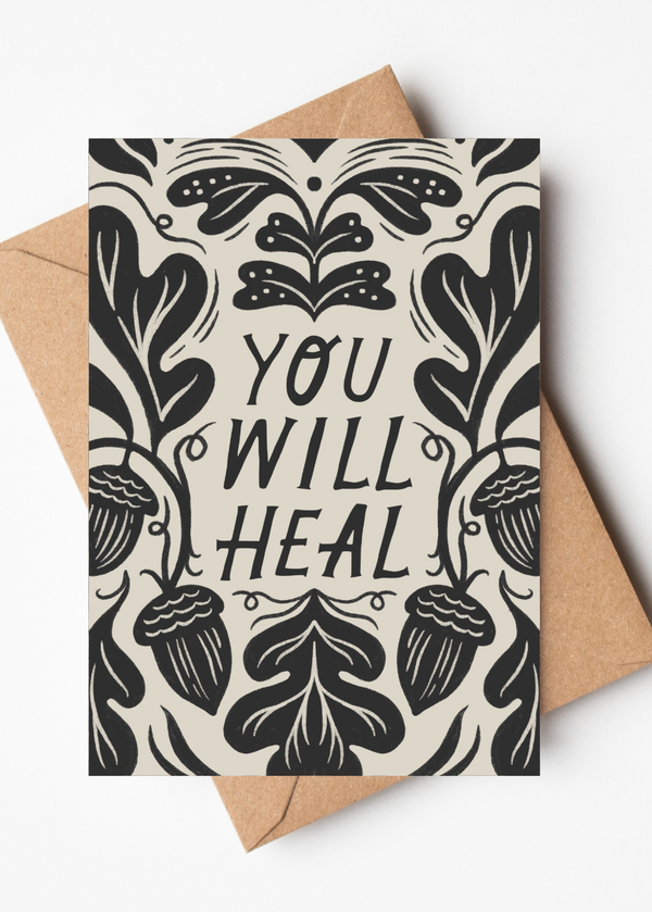 A square greeting card with a black botanical illustration and the words 'YOU WILL HEAL' in the center, shown with a kraft paper envelope on a light gray background.