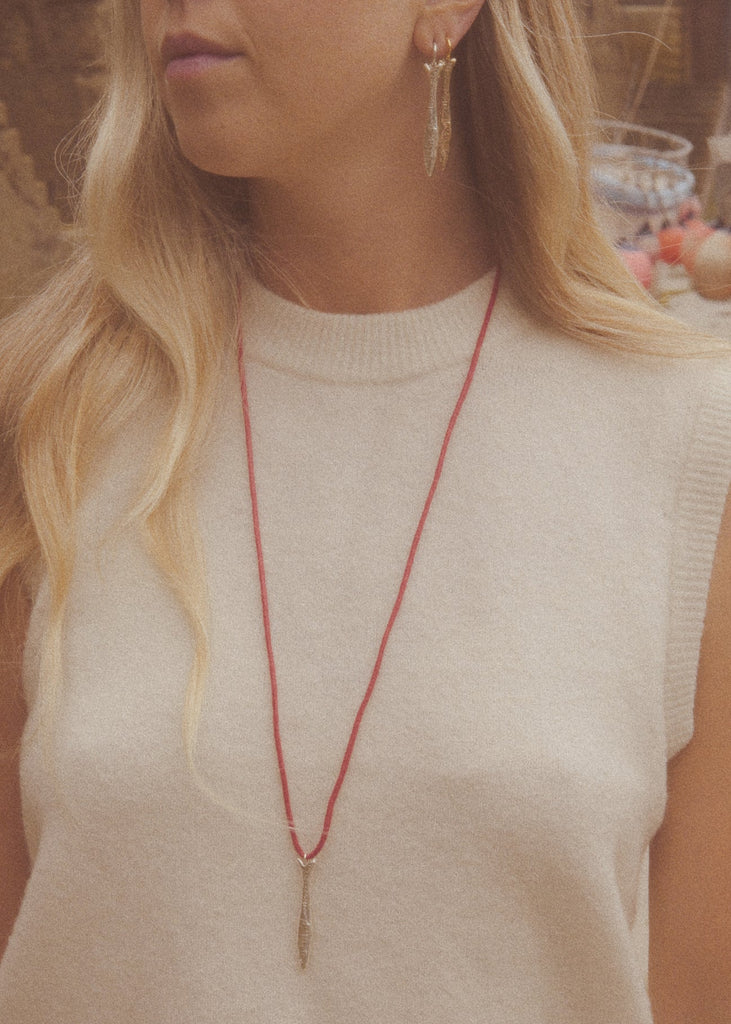 Woman wearing a red necklace and beige sleeveless top outdoors