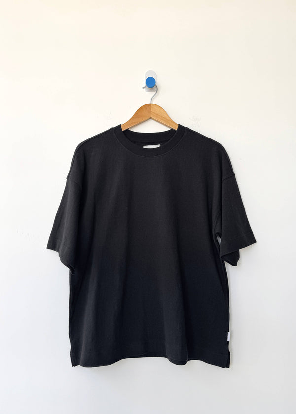 Black t-shirt on a wooden hanger against a white background