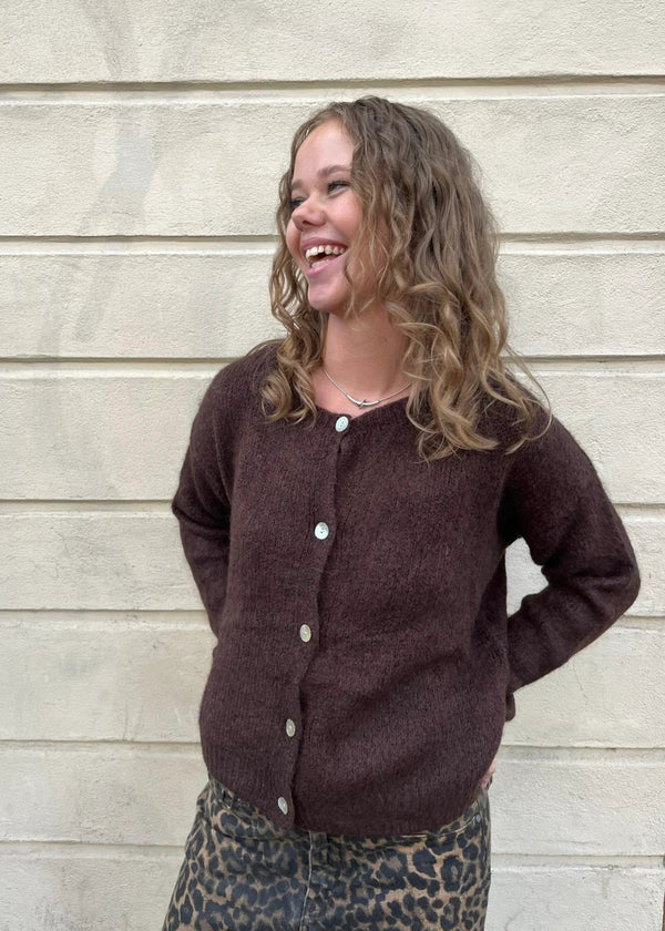 Woman wearing a brown cardigan standing against a beige wall