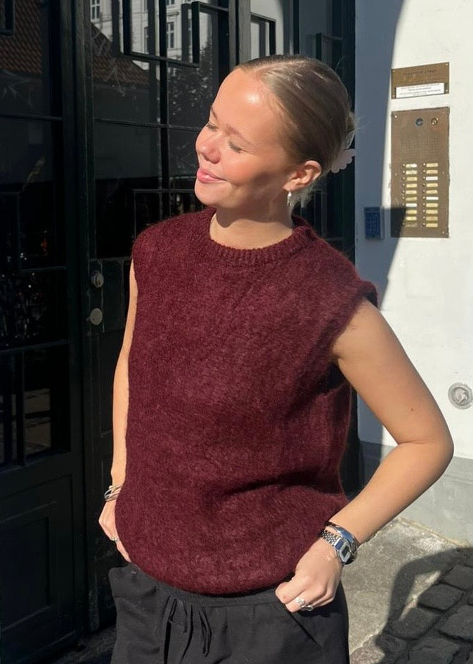 Woman wearing a burgundy sleeveless sweater standing outside a building.