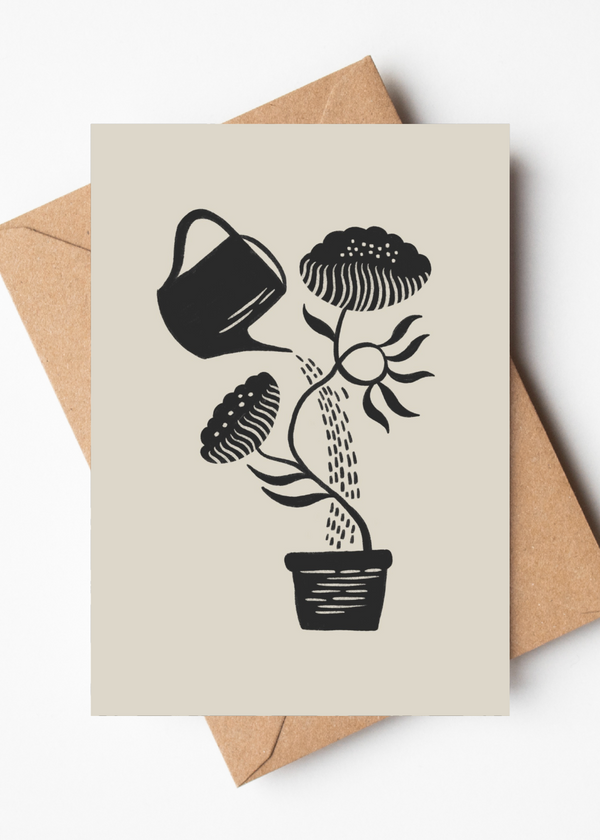 A beige greeting card with a black woodcut-style illustration of a potted plant being watered by a watering can, shown with a brown kraft envelope on a white background.