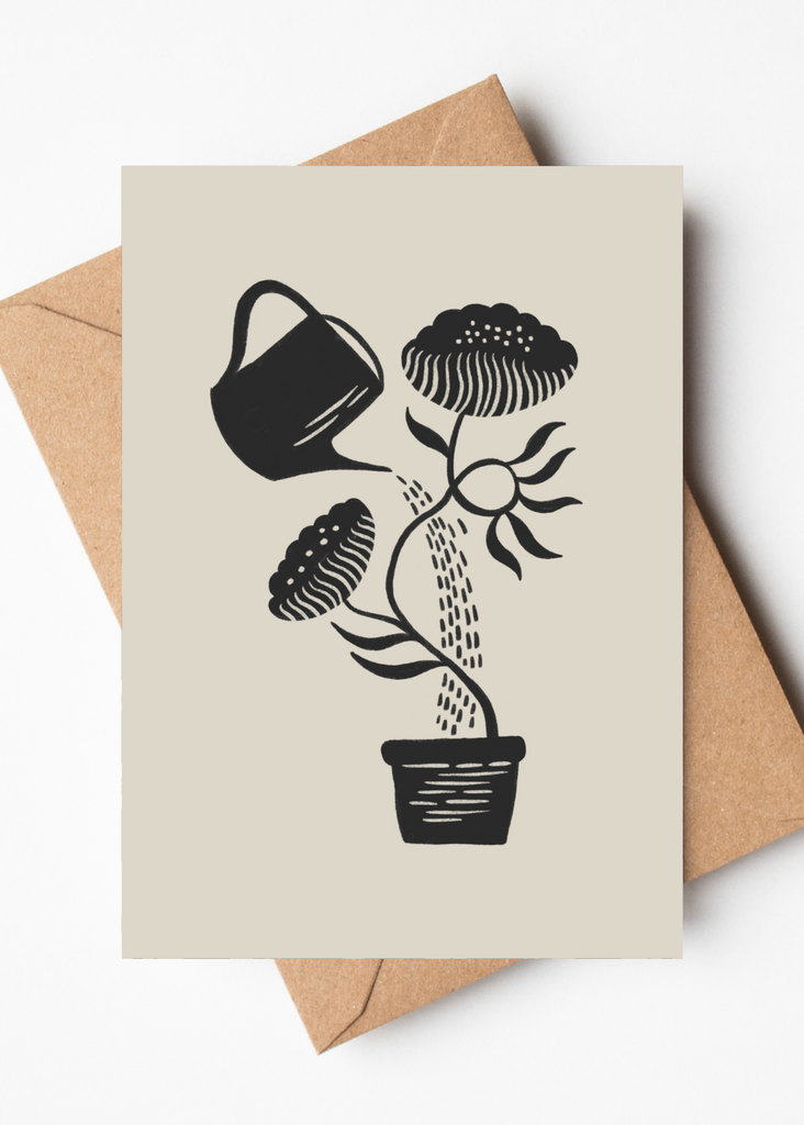 A beige greeting card with a black woodcut-style illustration of a potted plant being watered by a watering can, shown with a brown kraft envelope on a white background.