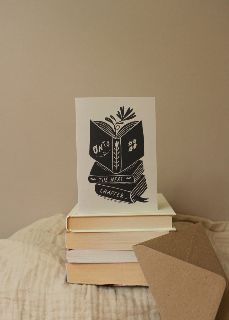 Stack of books with a card on top featuring text and an illustration, against a beige background.