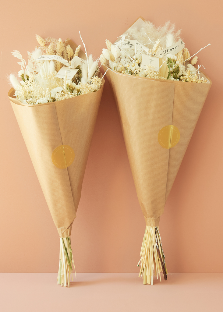 Two flower bouquets wrapped in brown paper with gold dots on a peach background