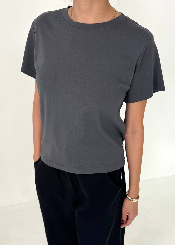 Person wearing a plain dark gray t-shirt and black pants on a white background