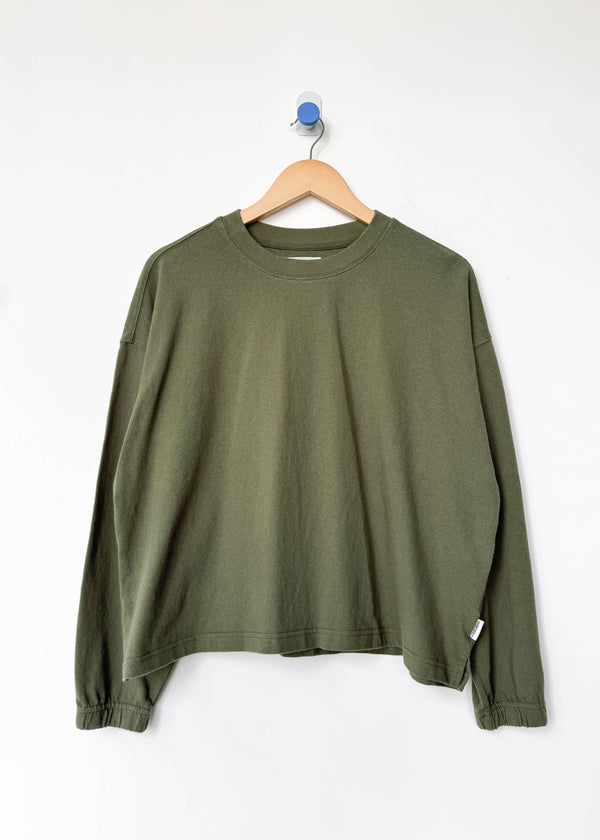Green long-sleeve shirt on a wooden hanger against a white background