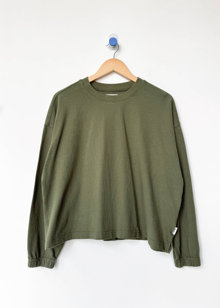 Green long-sleeve shirt on a wooden hanger against a white background