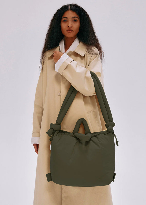 Woman holding a green bag against a plain background