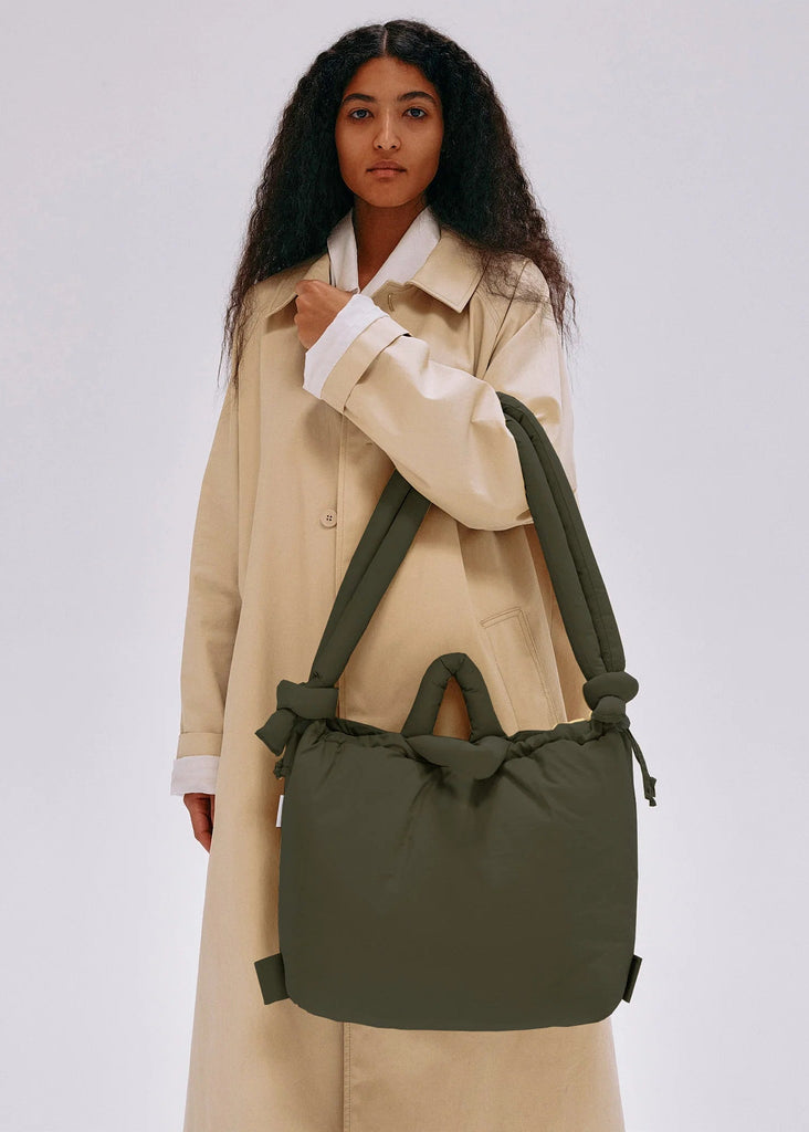 Woman holding a green bag against a plain background