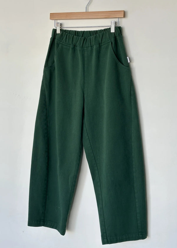 Green pants hanging on a wooden hanger against a white wall