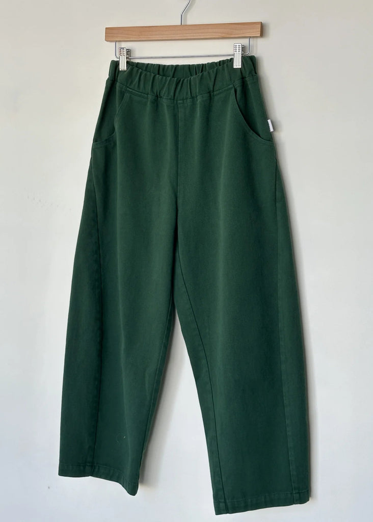 Green pants hanging on a wooden hanger against a white wall