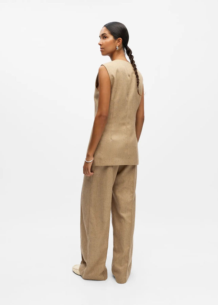 Woman wearing a beige sleeveless top and pants on a white background