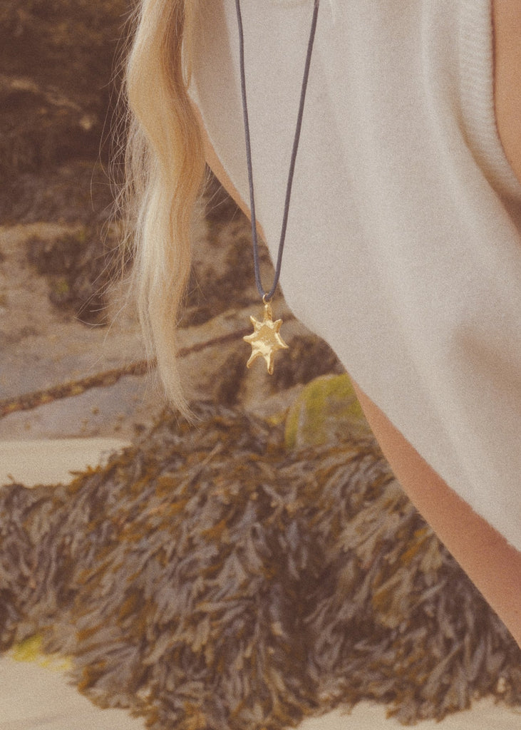 Close-up of a necklace with a star pendant worn by a person against a natural background.