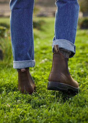Brown boots worn with rolled-up blue jeans on a grassy surface
