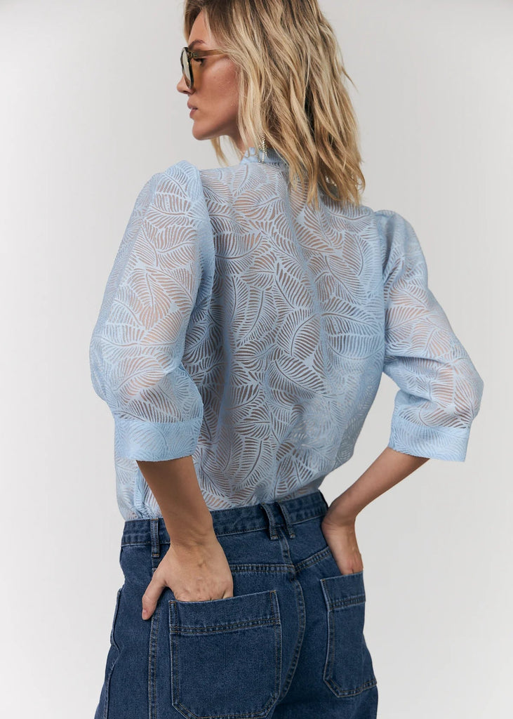 Woman wearing a light blue lace blouse and dark blue jeans against a white background