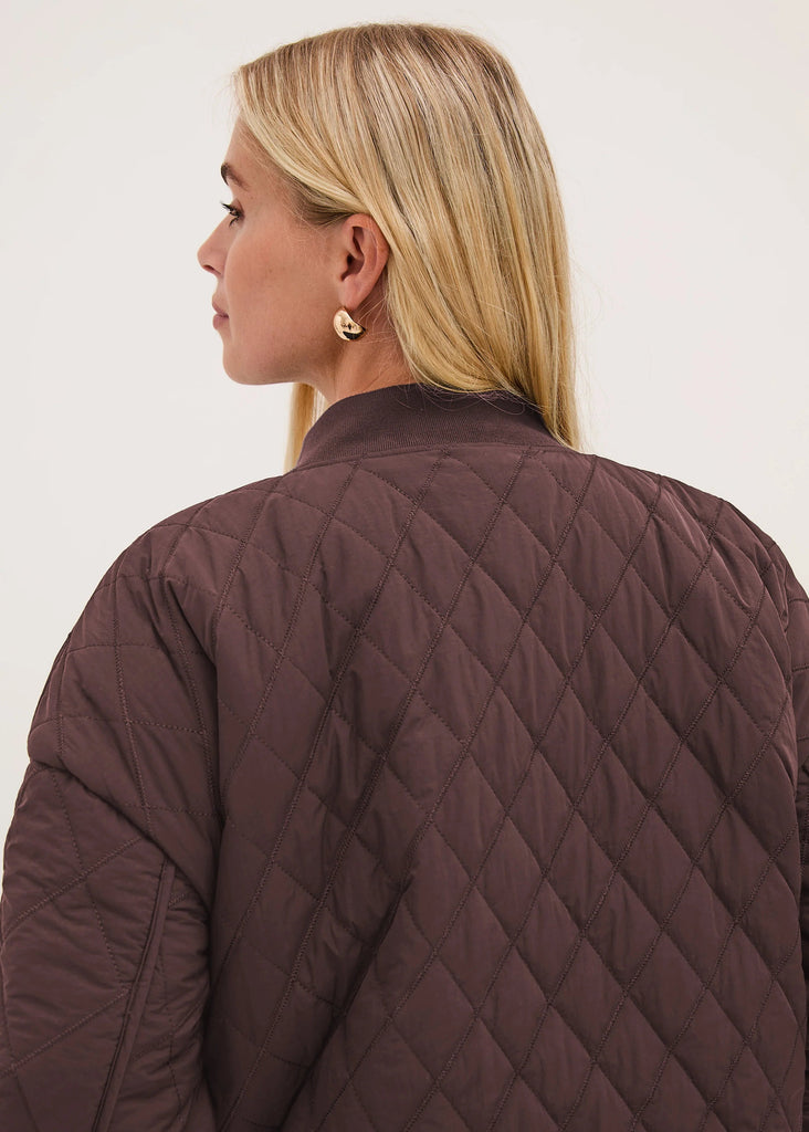 A woman shown from the back wearing a dark brown diamond-quilted jacket against a plain light background.