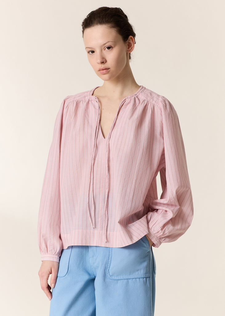 Woman wearing a pink blouse and blue pants against a beige background