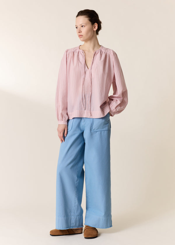 Person wearing a pink blouse and light blue pants on a beige background