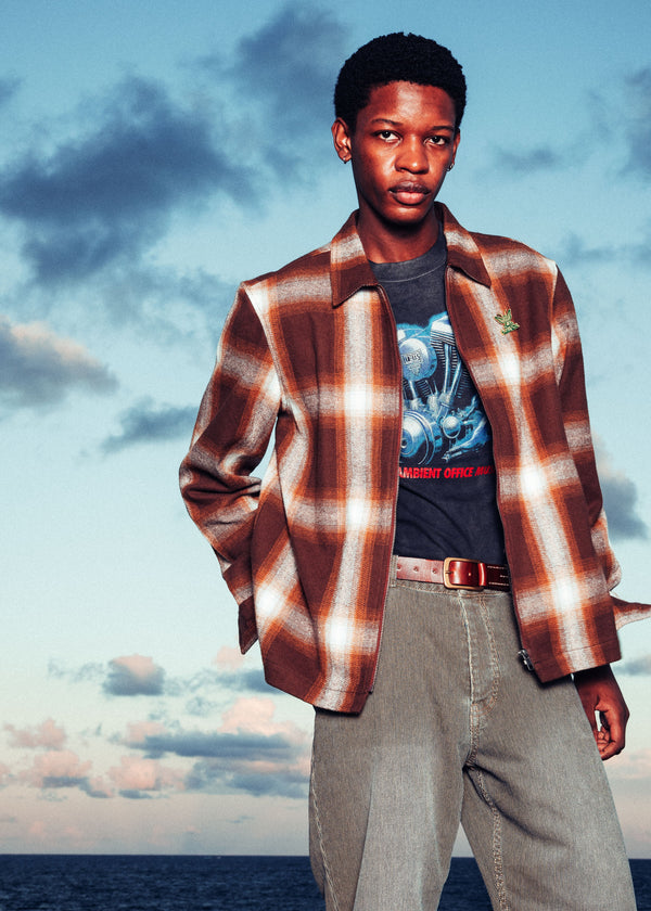 Man wearing a plaid shirt over a graphic t-shirt with a blue sky and ocean background
