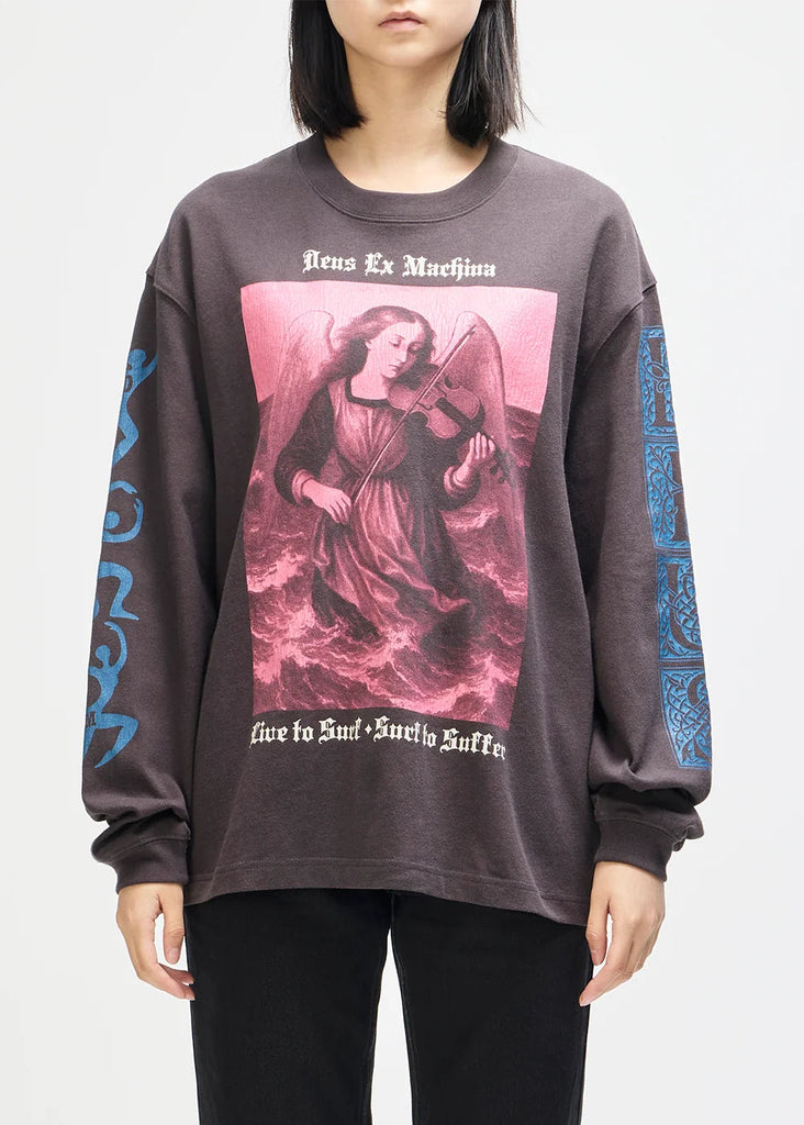 A model wearing a dark brown long-sleeve graphic t-shirt with a pink and red religious print on the front and blue gothic text on the sleeves, paired with black pants against a light gray background.