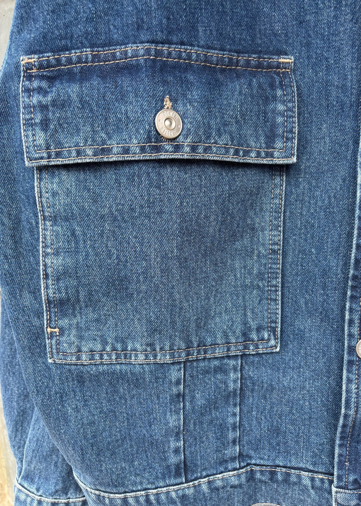 Close-up of a blue denim jacket with a buttoned pocket.