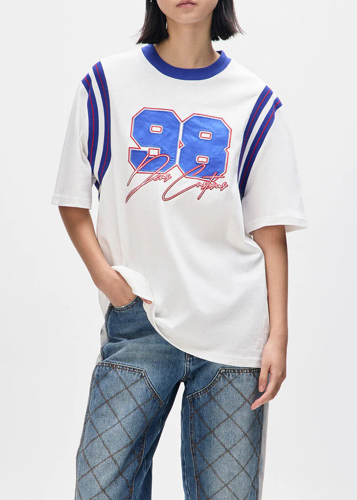 Person wearing a white t-shirt with blue and red design and blue jeans on a white background